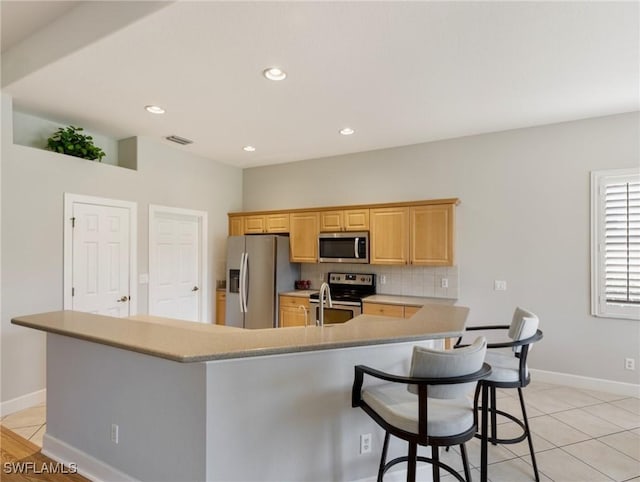 10230 Cobble Hill Rd, Bonita Springs, FL 34135 - kitchen featuring appliances with stainless steel finishes, light brown cabinetry, a breakfast bar area, light countertops, and backsplash