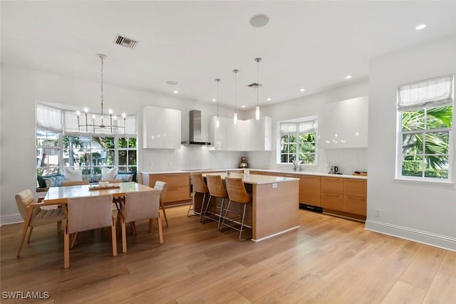 687 9th Ave S, Naples, FL 34102 - kitchen featuring wall chimney exhaust hood, modern cabinets, a center island, light wood-style floors, and light countertops