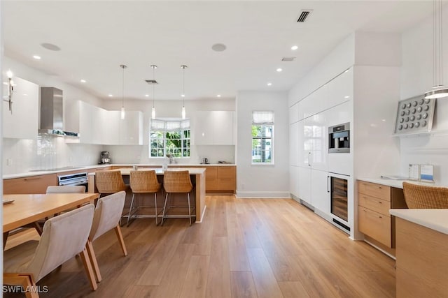687 9th Ave S, Naples, FL 34102 - kitchen with modern cabinets, wall chimney exhaust hood, light wood-style floors, a kitchen bar, and wine cooler