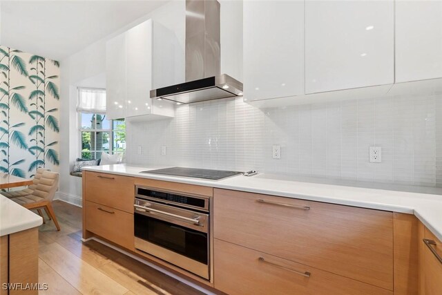 687 9th Ave S, Naples, FL 34102 - kitchen with wall chimney exhaust hood, oven, modern cabinets, light wood-type flooring, and light countertops