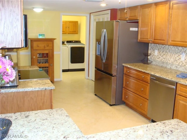 4802 Lakewood Blvd Unit B13, Naples, FL 34112 - kitchen featuring appliances with stainless steel finishes, washer and dryer, tasteful backsplash, brown cabinetry, and light stone counters
