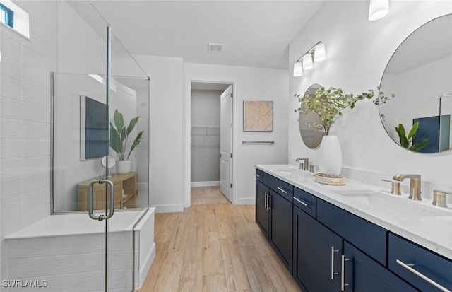 7049 Chapel Creek Ln, North Fort Myers, FL 33917 - bathroom featuring double vanity, a stall shower, wood finished floors, a walk in closet, and baseboards