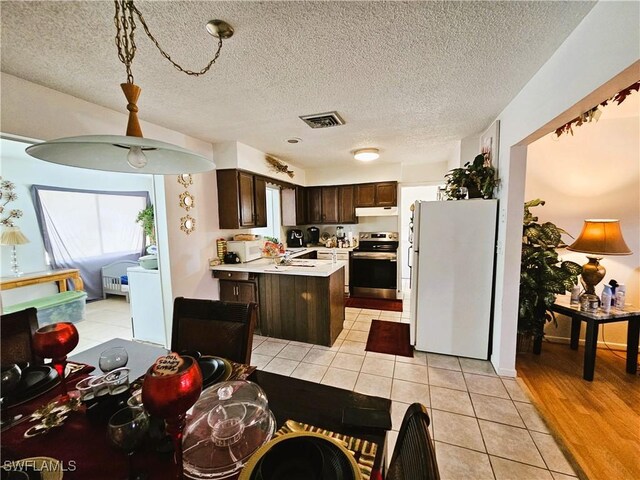 1112 Evanston St, Sebring, FL 33870 - kitchen with white appliances, light countertops, dark brown cabinetry, under cabinet range hood, and light tile patterned flooring