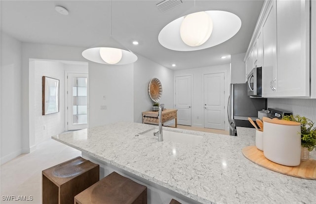6470 Memorial Ln, Ave Maria, FL 34142 - kitchen featuring stainless steel microwave, light stone countertops, recessed lighting, white cabinets, and a sink