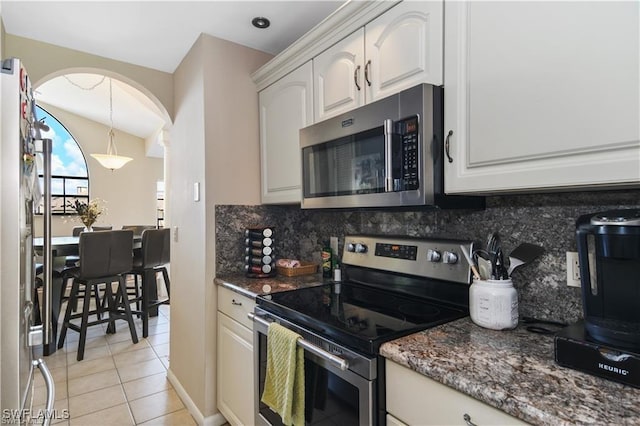 17260 Eagle Trce Unit 10, Fort Myers, FL 33908 - kitchen featuring stainless steel appliances, arched walkways, decorative backsplash, light tile patterned floors, and dark stone counters