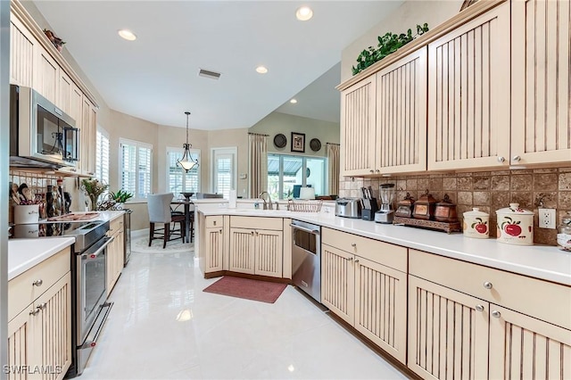 3181 Bramble Cove Ct, Fort Myers, FL 33905 - kitchen with appliances with stainless steel finishes, cream cabinets, a peninsula, tasteful backsplash, and pendant lighting