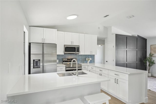 4906 5th St W, Lehigh Acres, FL 33971 - kitchen featuring appliances with stainless steel finishes, a peninsula, a sink, vaulted ceiling, and tasteful backsplash