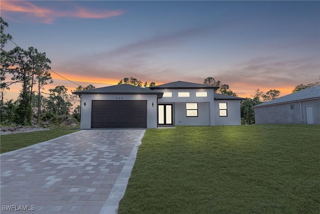 view of front of property featuring decorative driveway, a lawn, a garage, and stucco siding