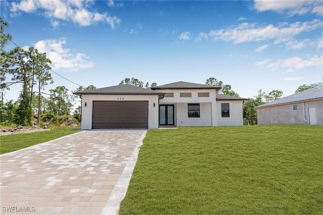 prairie-style home featuring decorative driveway, a front yard, and stucco siding