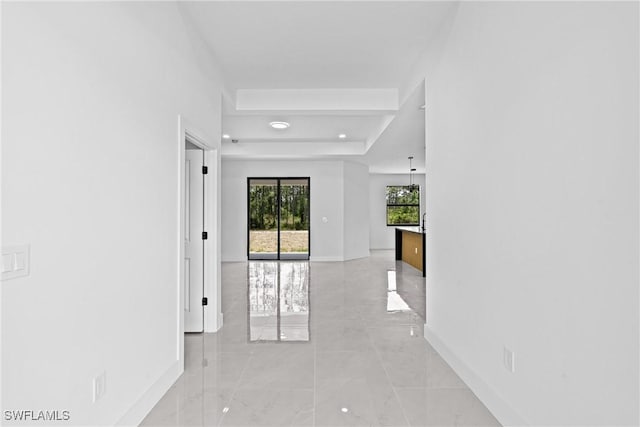 corridor featuring baseboards, a raised ceiling, and light marble finish floors