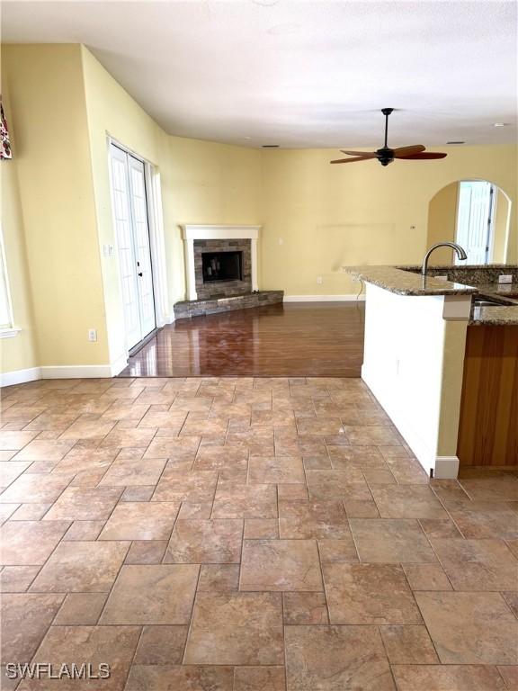4150 Enclave Pl, Punta Gorda, FL 33980 - unfurnished living room with a stone fireplace, ceiling fan, arched walkways, a sink, and baseboards