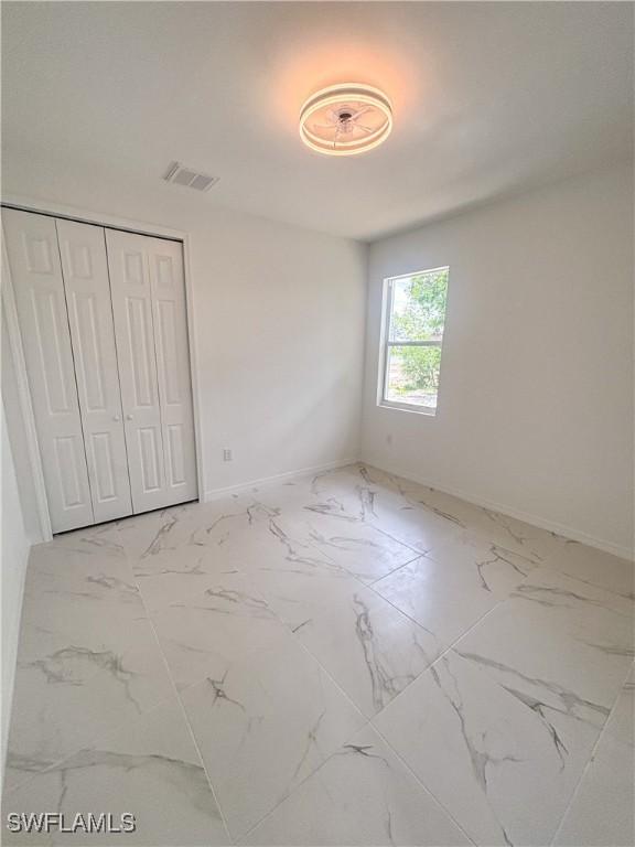3806 15th St W, Lehigh Acres, FL 33971 - unfurnished bedroom featuring marble look tiles, baseboards, and a closet