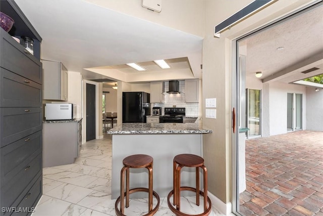 1704 Coral Way N, Fort Myers, FL 33917 - kitchen with black appliances, wall chimney range hood, a peninsula, light stone countertops, and a breakfast bar