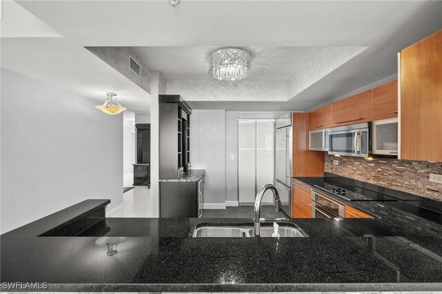 3000 Oasis Grand Blvd Unit 2103, Fort Myers, FL 33916 - kitchen featuring stainless steel microwave, built in fridge, black electric cooktop, tasteful backsplash, and brown cabinetry