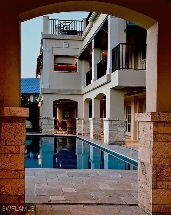 2001 4th St S, Naples, FL 34102 - back of property with stucco siding, an outdoor pool, a patio area, a balcony, and stone siding