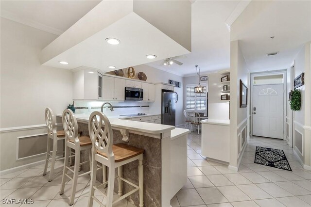 14550 Red Fox Run Unit 407, Naples, FL 34110 - kitchen with stainless steel appliances, a peninsula, light countertops, white cabinets, and ornamental molding