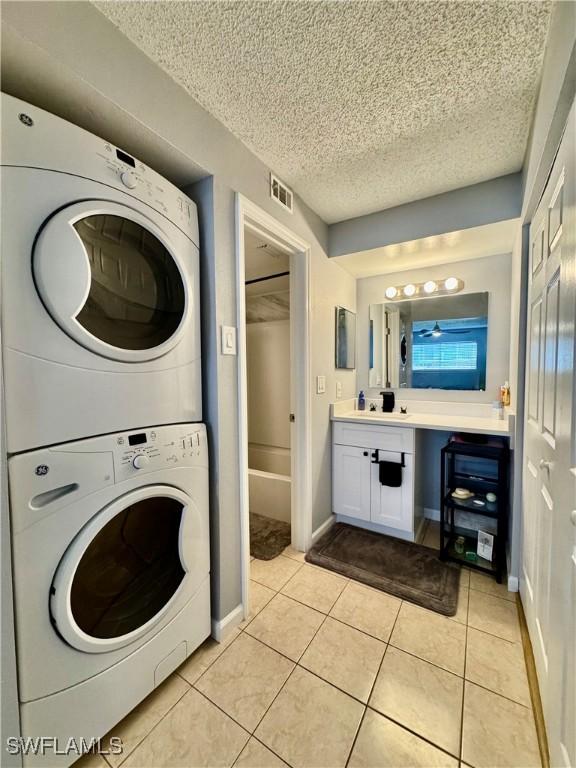 5751 Foxlake Dr Unit A, North Fort Myers, FL 33917 - laundry room with stacked washer and clothes dryer, a textured ceiling, light tile patterned floors, and baseboards