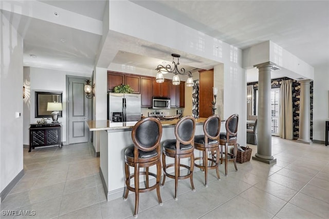 23159 Amgci Way Unit 302, Estero, FL 33928 - kitchen featuring appliances with stainless steel finishes, decorative columns, light tile patterned floors, a breakfast bar area, and a peninsula