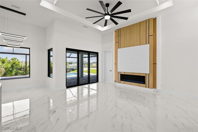 220 NE 6th St, Cape Coral, FL 33909 - empty room featuring a tray ceiling, marble tiled floors, a ceiling fan, a tiled fireplace, and a high ceiling