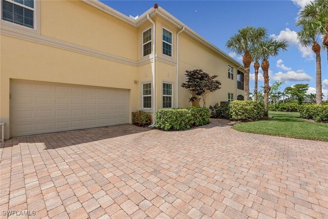 1263 Rialto Way Unit 102, Naples, FL 34114 - view of home's exterior featuring stucco siding, decorative driveway, a garage, and a lawn