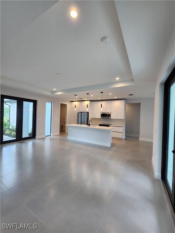 3279 31st Ave NE, Naples, FL 34120 - unfurnished living room featuring a tray ceiling, baseboards, plenty of natural light, and recessed lighting