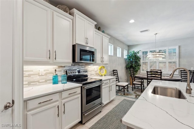 14559 Topsail Dr, Naples, FL 34114 - kitchen featuring stainless steel appliances, a sink, backsplash, white cabinetry, and a chandelier