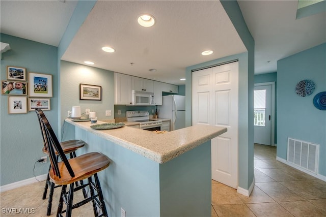 16641 Stringfellow Rd Unit 506, Bokeelia, FL 33922 - kitchen with white appliances, light tile patterned floors, a kitchen bar, a peninsula, and baseboards