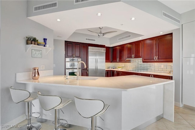 1050 Borghese Ln Unit 801, Naples, FL 34114 - kitchen with reddish brown cabinets, appliances with stainless steel finishes, a tray ceiling, a kitchen bar, and backsplash