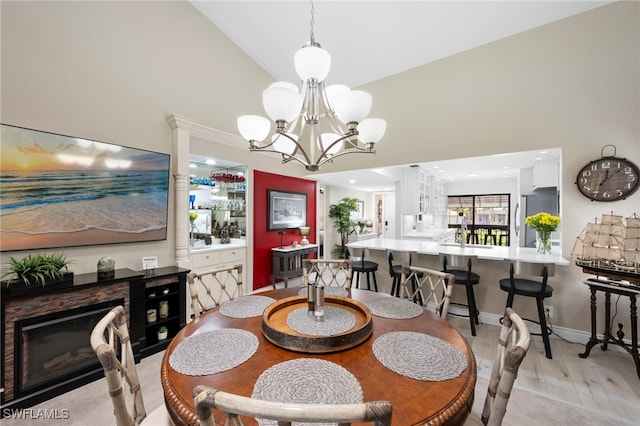 15444 Admiralty Cir Unit 10, North Fort Myers, FL 33917 - dining room with a chandelier, light wood-style flooring, a glass covered fireplace, high vaulted ceiling, and ornate columns