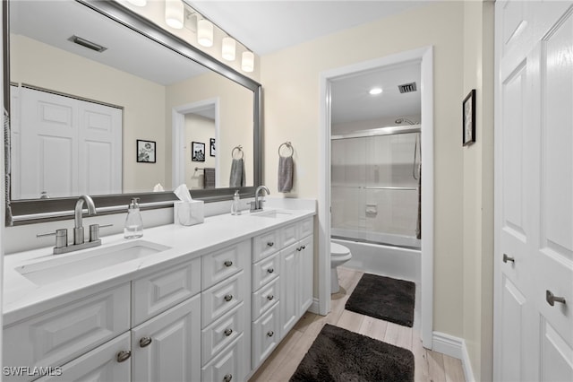 15444 Admiralty Cir Unit 10, North Fort Myers, FL 33917 - bathroom featuring toilet, double vanity, combined bath / shower with glass door, and wood finished floors