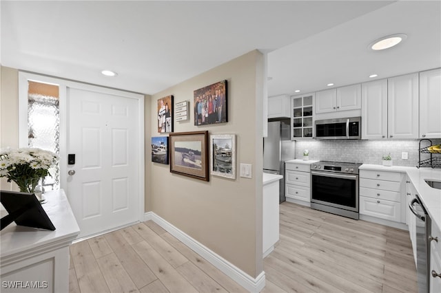 15444 Admiralty Cir Unit 10, North Fort Myers, FL 33917 - kitchen with stainless steel appliances, baseboards, light wood-style flooring, white cabinets, and decorative backsplash