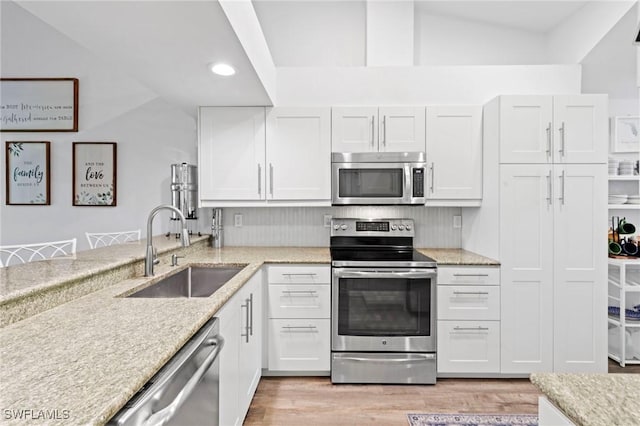 10811 Breaker Ln, Naples, FL 34109 - kitchen featuring stainless steel appliances, a sink, vaulted ceiling, light wood-style flooring, and white cabinets