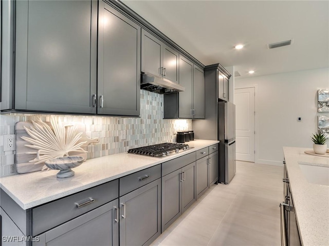 17304 Green Buttonwood Way N, Fort Myers, FL 33917 - kitchen with under cabinet range hood, appliances with stainless steel finishes, decorative backsplash, baseboards, and gray cabinets