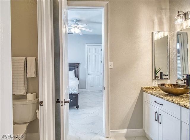 623 SW 56th St, Cape Coral, FL 33914 - bathroom with marble look tiles, vanity, toilet, ceiling fan, and baseboards