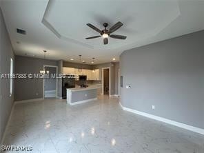 426 Mercedes Ct, Lehigh Acres, FL 33972 - unfurnished living room with baseboards, a ceiling fan, light marble finish flooring, and a raised ceiling