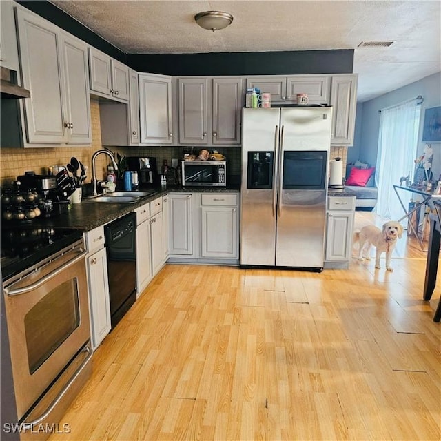 3411 22nd St SW, Lehigh Acres, FL 33976 - kitchen featuring appliances with stainless steel finishes, dark countertops, a sink, tasteful backsplash, and light wood-type flooring
