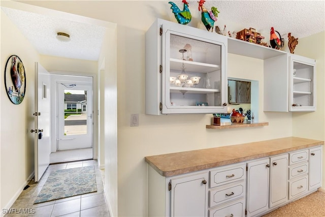 6843 Bogey Dr, Fort Myers, FL 33919 - kitchen featuring a textured ceiling, glass insert cabinets, baseboards, light tile patterned floors, and white cabinetry