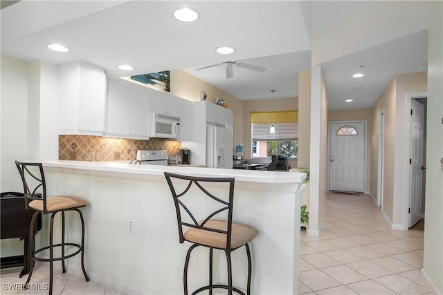 6810 Beach Resort Dr Unit 13, Naples, FL 34114 - kitchen featuring white appliances, a peninsula, a breakfast bar, ceiling fan, and decorative backsplash