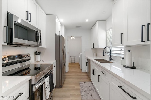 4126 Belair Ln Unit C6, Naples, FL 34103 - kitchen featuring appliances with stainless steel finishes, a sink, light wood finished floors, white cabinetry, and washer / clothes dryer