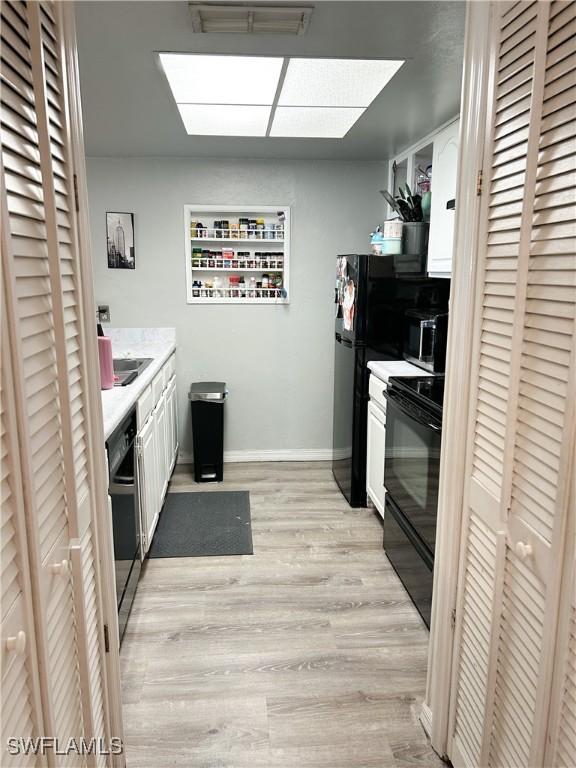 3062 Kings Lake Blvd Unit 7511, Naples, FL 34112 - kitchen with black appliances, white cabinetry, light countertops, light wood finished floors, and a skylight