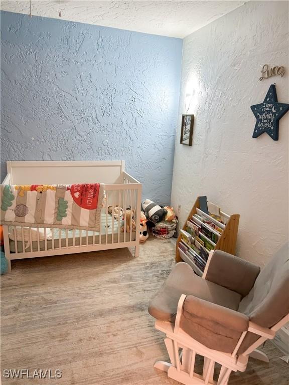 3062 Kings Lake Blvd Unit 7511, Naples, FL 34112 - bedroom with a textured wall, a nursery area, and wood finished floors
