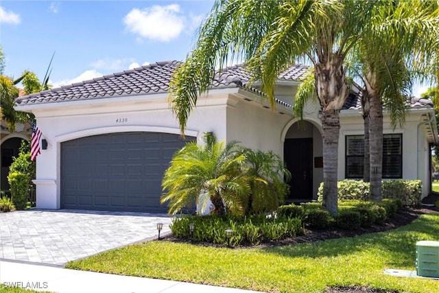 4330 Aurora St, Naples, FL 34119 - mediterranean / spanish house with stucco siding, an attached garage, a tiled roof, decorative driveway, and a front lawn