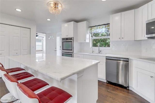 2940 14th Ave SE, Naples, FL 34117 - kitchen with stainless steel appliances, dark wood-style flooring, tasteful backsplash, a breakfast bar area, and white cabinetry