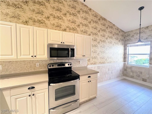 8088 Sanctuary Dr Unit 1, Naples, FL 34104 - kitchen featuring stainless steel appliances, wallpapered walls, lofted ceiling, light countertops, and light wood finished floors