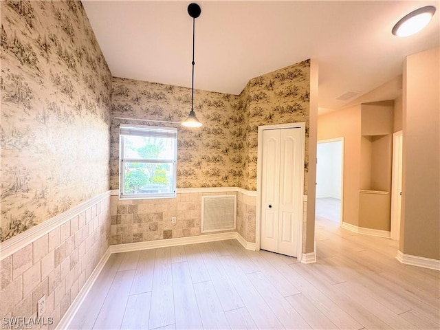 8088 Sanctuary Dr Unit 1, Naples, FL 34104 - unfurnished dining area featuring wallpapered walls, wood finished floors, a wainscoted wall, and lofted ceiling
