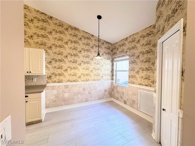 8088 Sanctuary Dr Unit 1, Naples, FL 34104 - unfurnished dining area featuring wallpapered walls, a wainscoted wall, light wood-type flooring, and lofted ceiling