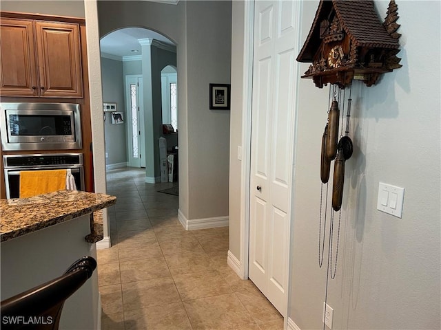 11010 Longwing Dr, Fort Myers, FL 33912 - kitchen with stainless steel appliances, ornamental molding, arched walkways, light tile patterned floors, and brown cabinets