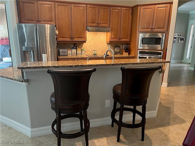 11010 Longwing Dr, Fort Myers, FL 33912 - kitchen featuring stainless steel appliances, dark stone counters, a kitchen breakfast bar, brown cabinets, and crown molding