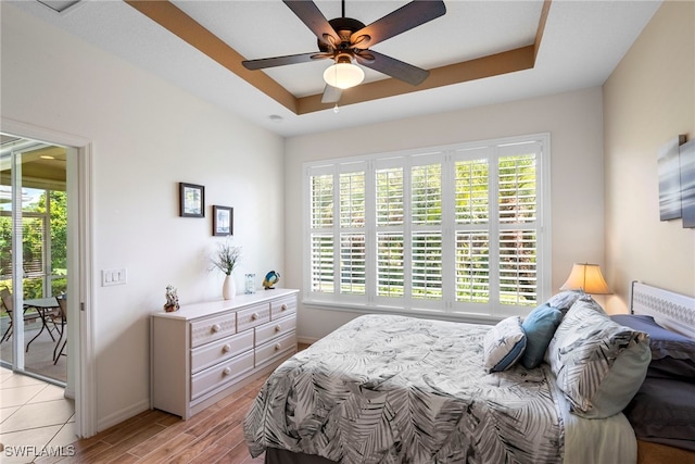 bedroom with multiple windows, a raised ceiling, light wood-type flooring, and access to outside