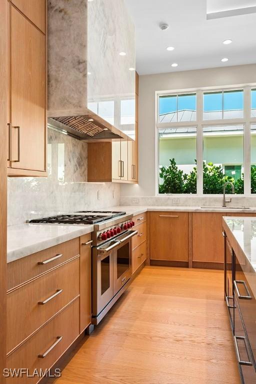 777 Broad Ct S, Naples, FL 34102 - kitchen with wall chimney range hood, range with two ovens, a sink, light wood-style floors, and decorative backsplash